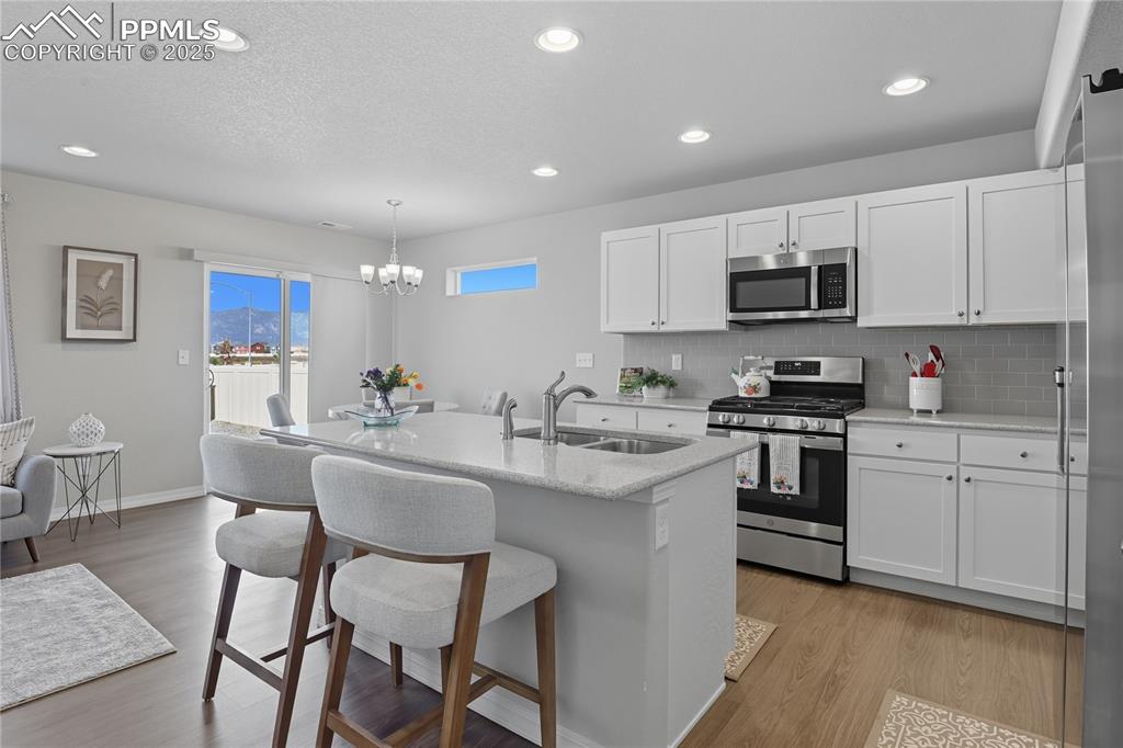 KITCHEN FEATURES SLEEK WHITE CABINETRY, STAINLESS STEEL APPLIANCES, AND A BREAKFAST BAR