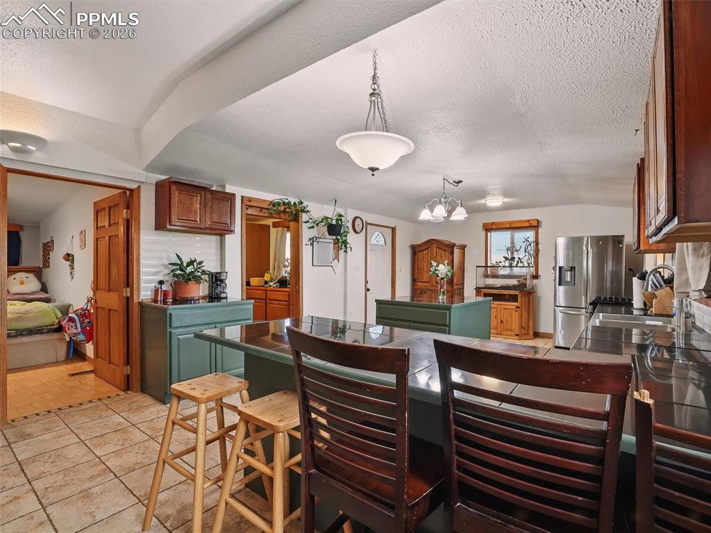 Kitchen with dark countertops, pendant lighting, a breakfast bar area, stainless steel fridge with ice dispenser, and a kitchen island