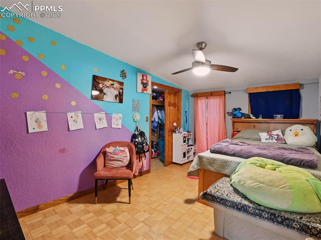 Bedroom with parquet floors, a ceiling fan, a closet, and a textured wall