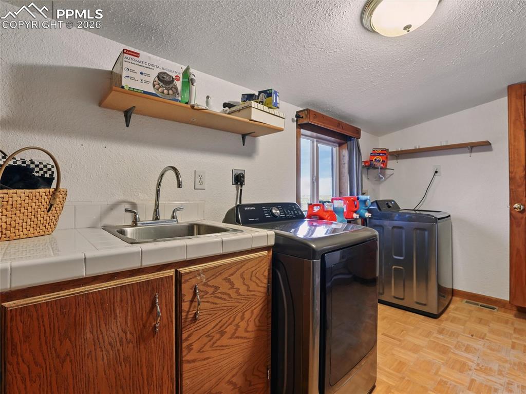 Laundry room featuring parquet flooring, cabinet space, washing machine and clothes dryer, and a textured ceiling