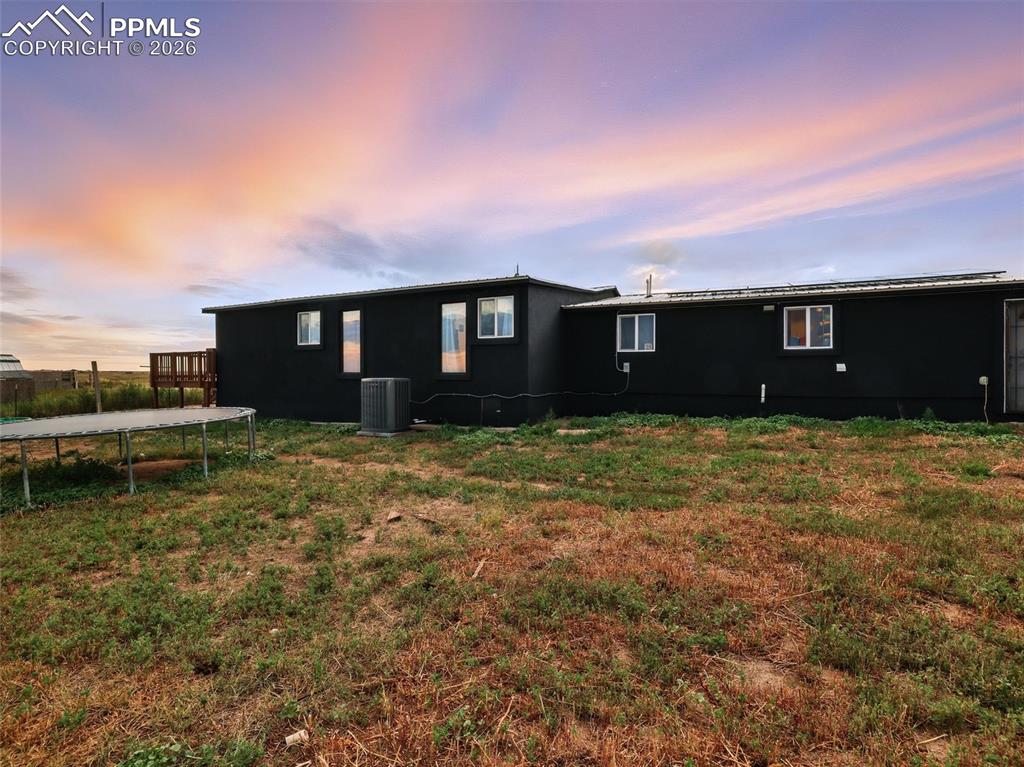 Back of property at dusk featuring a trampoline and a lawn