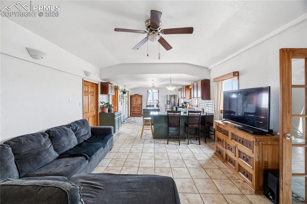 Living room featuring ceiling fan, vaulted ceiling, light tile patterned floors, and a textured wall