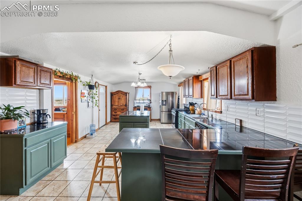 Kitchen with dark countertops, a kitchen bar, stainless steel appliances, a kitchen island, and light tile patterned floors