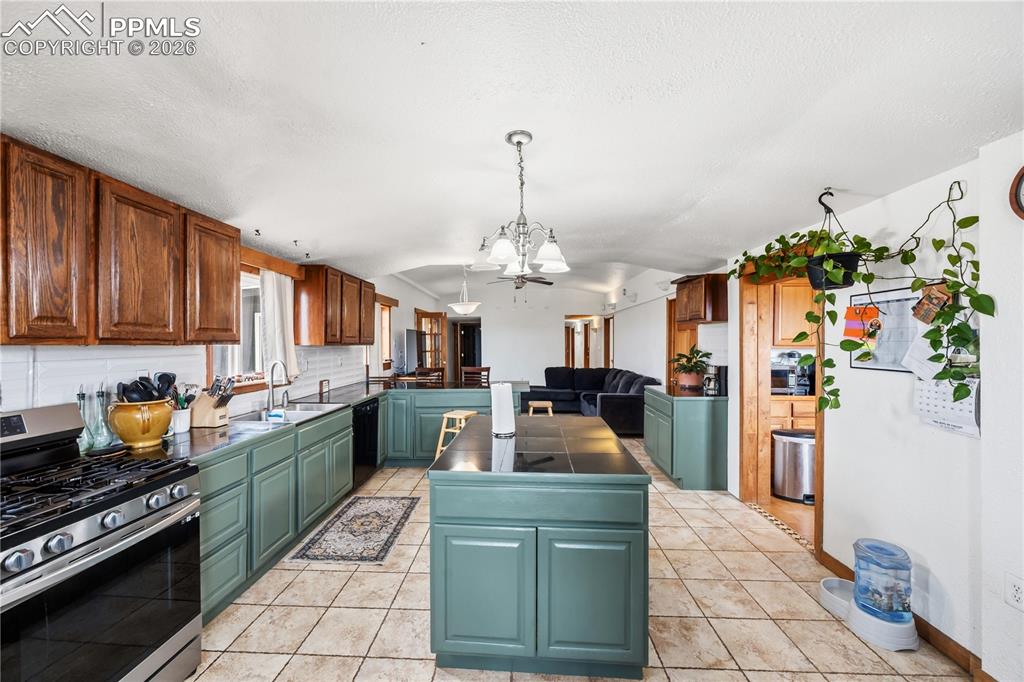Kitchen featuring stainless steel range with gas stovetop, dark countertops, a kitchen island, a chandelier, and a peninsula