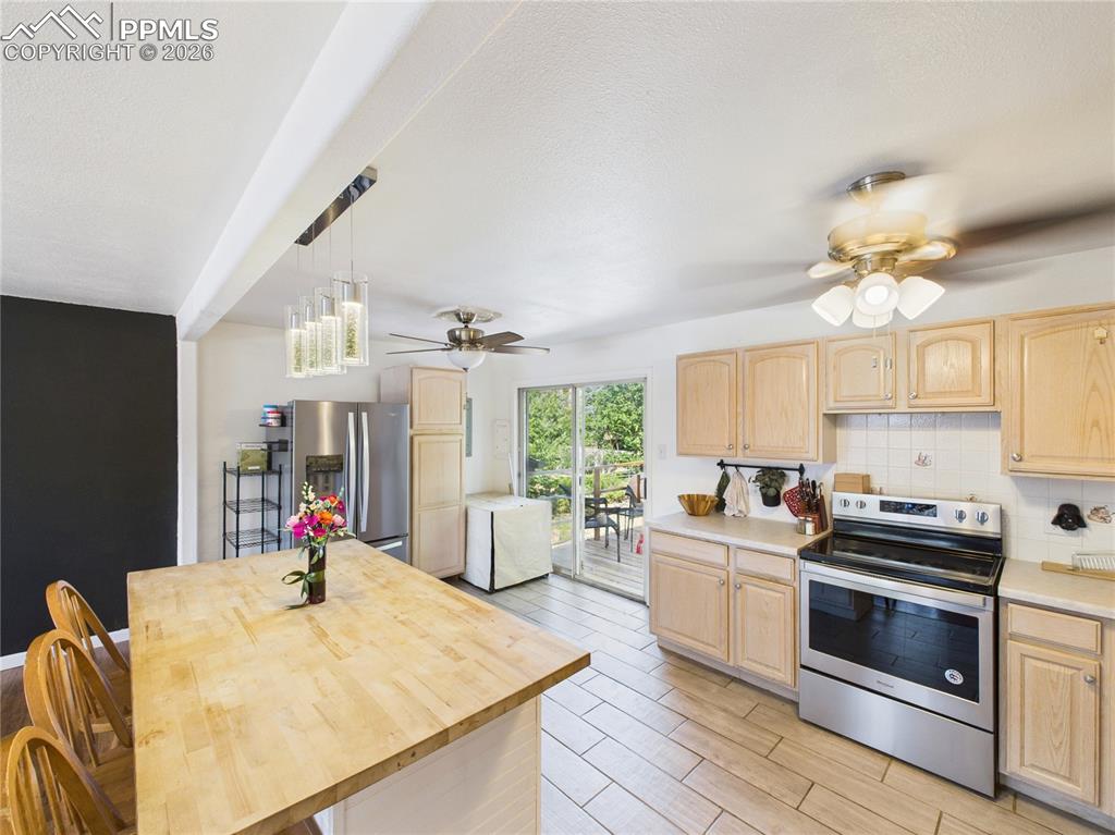 Kitchen with light wood finish cabinets, stainless steel appliances, a ceiling fan, tasteful backsplash, and a textured ceiling