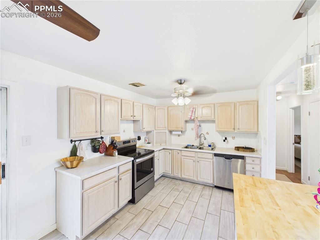 Kitchen featuring light wood finish cabinets, butcher block counters, stainless steel appliances, ceiling fan, and wood finish floors