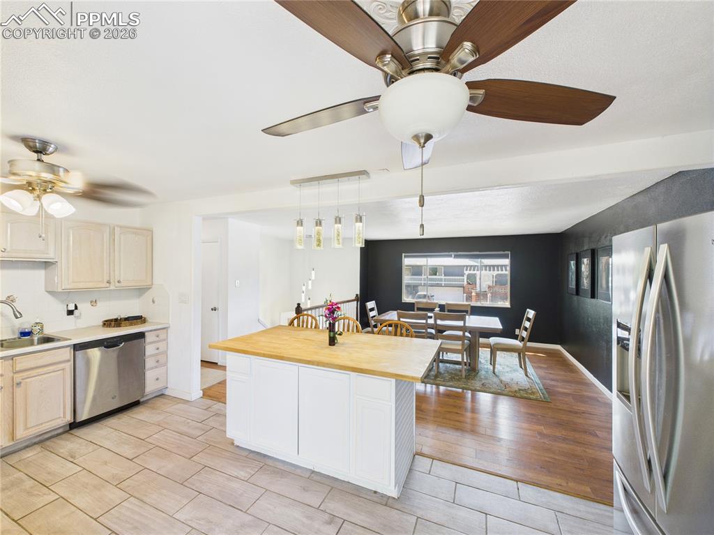 Kitchen with stainless steel appliances, a ceiling fan, butcher block counters, wood tiled floors, and pendant lighting
