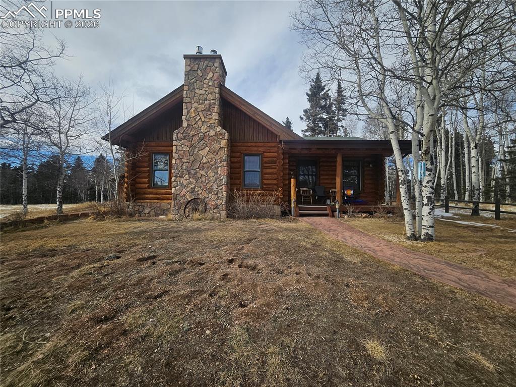 The cabin  with log exterior, covered porch, and a stone chimney