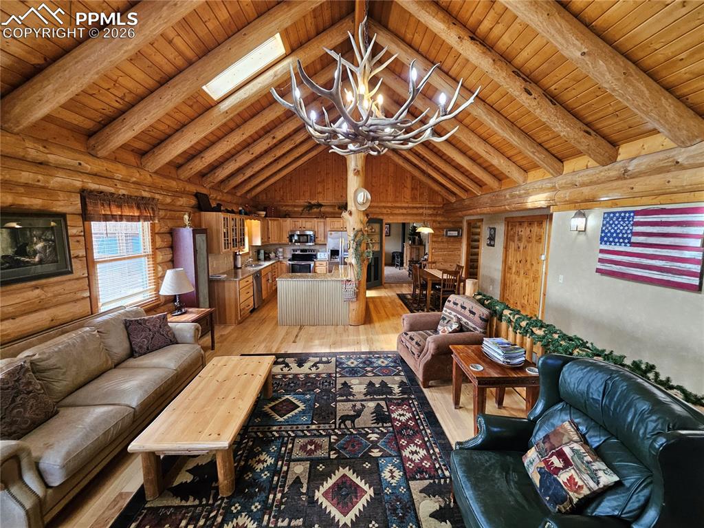 Cabin living area featuring log walls, suspended lighting, light wood-type flooring, a wood ceiling with exposed beams, and skylights