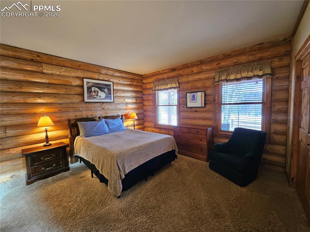 Cabin primary bedroom featuring carpet flooring and rustic log wood walls
