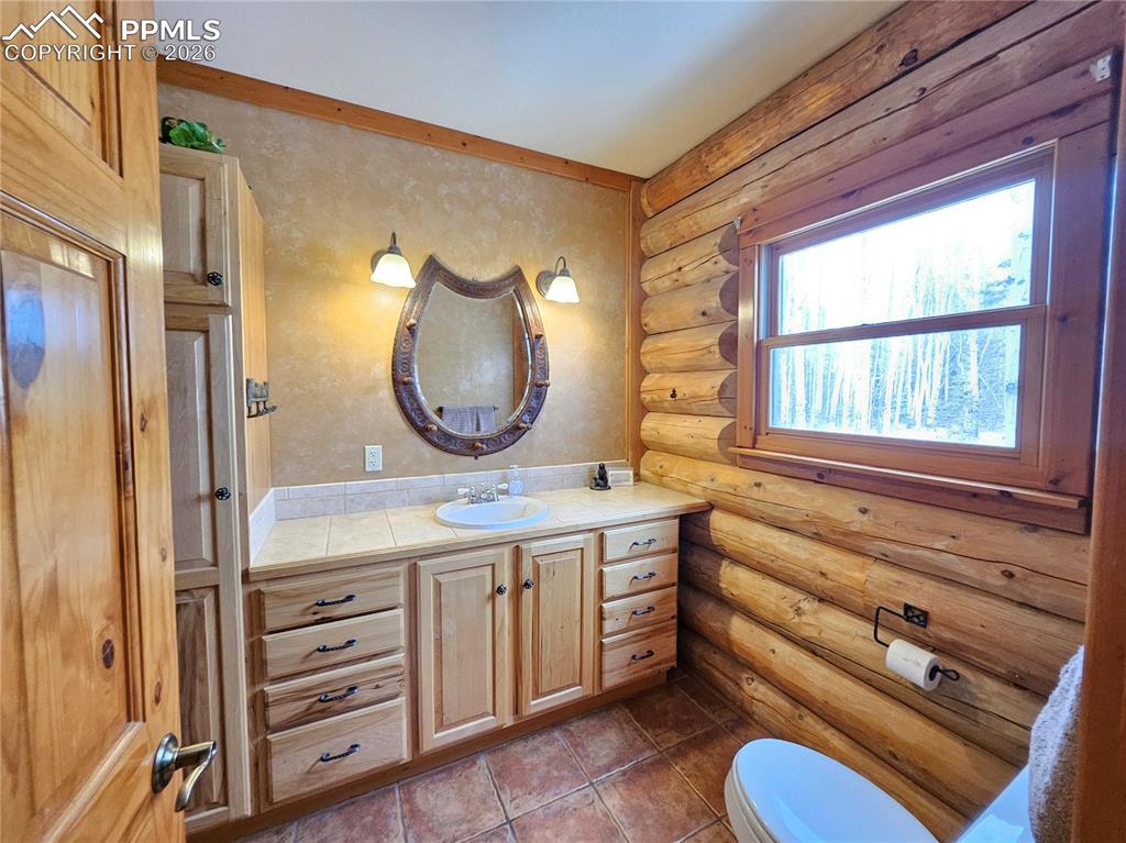 Cabin primary bathroom featuring log walls, vanity, and dark tile patterned flooring