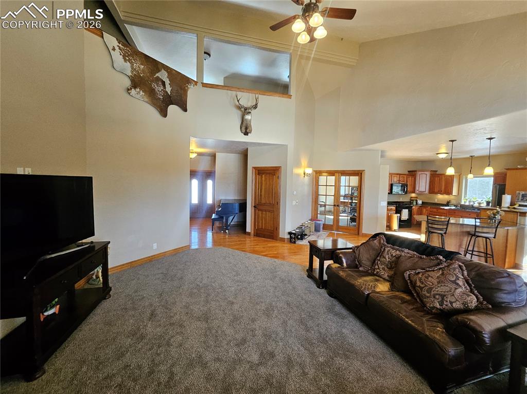 Living area with French doors, light colored carpet, ceiling fan, plenty of natural light, and a high ceiling