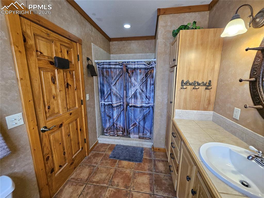 Bathroom featuring a shower stall, vanity, ornamental molding, and dark tile patterned flooring