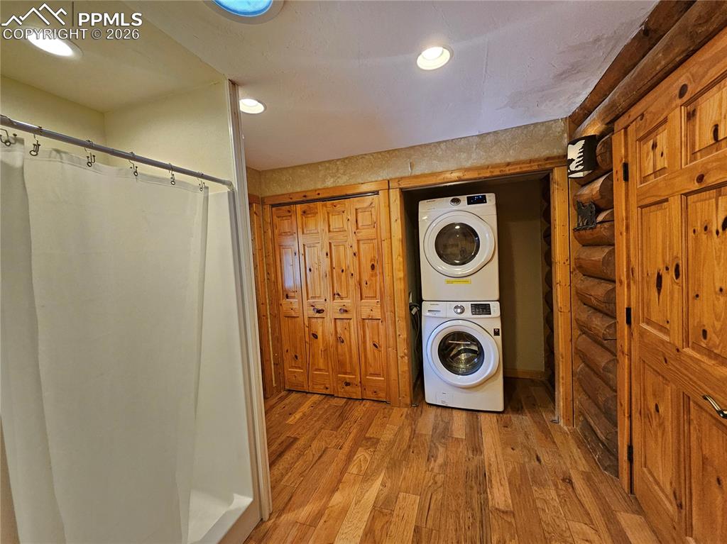 Cabin laundry area featuring hardwood / wood-style flooring, stacked washing machine and dryer, log walls, and recessed lighting