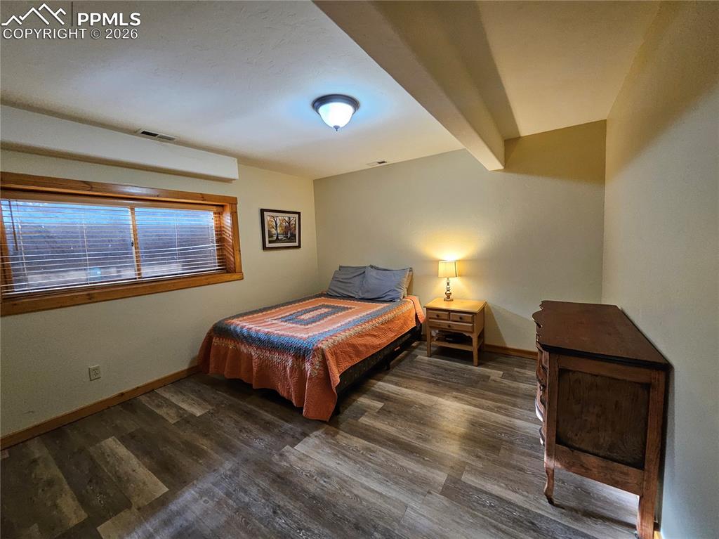 Cabin bedroom in basement featuring beam ceiling and dark wood-style flooring