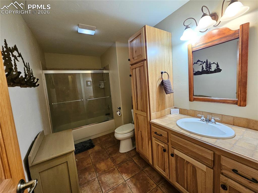 Cabin basement full bathroom featuring vanity, shower / bath combination with glass door, and dark tile patterned floors