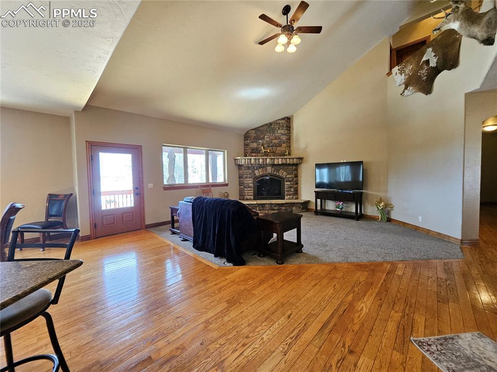 Living room featuring ceiling fan, light wood-style flooring, vaulted ceiling, and a stone fireplace