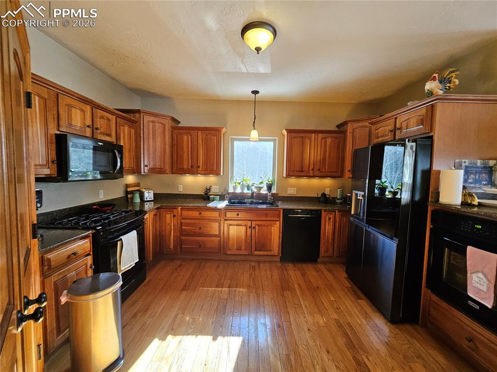 Kitchen with wood finish cabinetry, black appliances, hanging light fixtures, and dark granite countertops