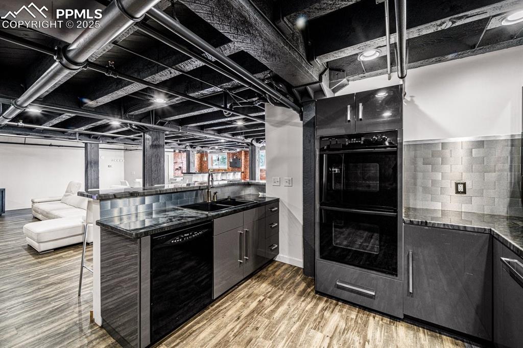 Kitchen featuring black appliances, wood finished floors, a breakfast bar area, a peninsula, and dark cabinetry