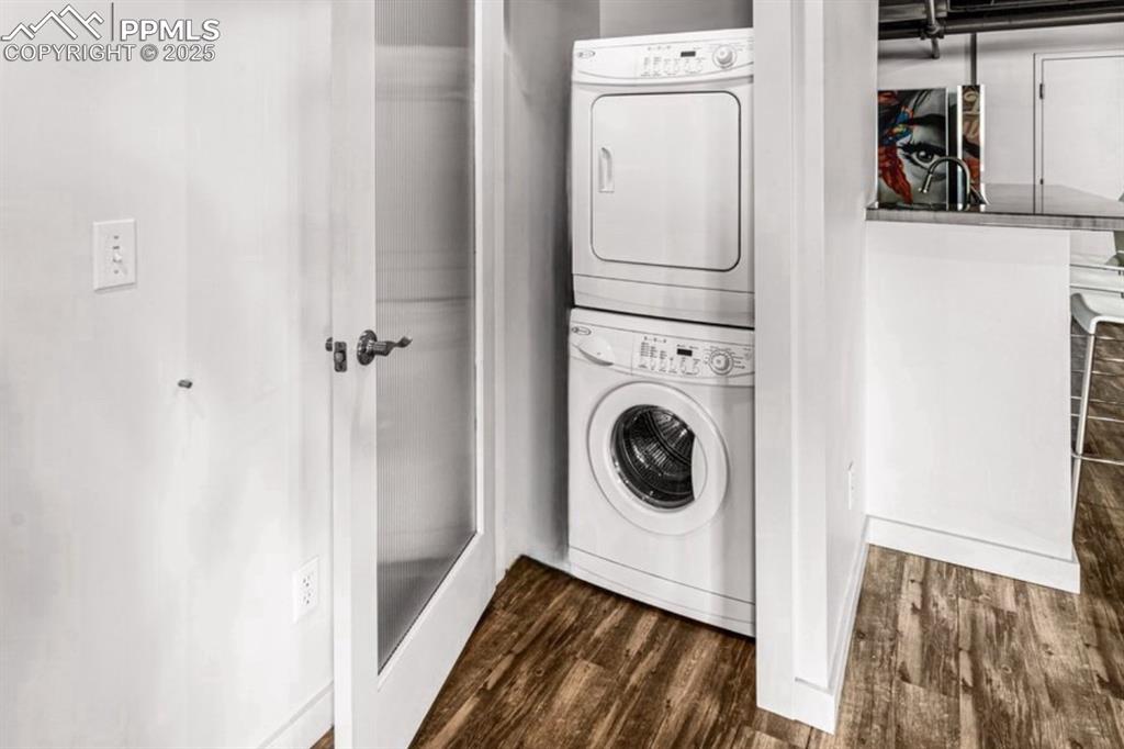 Laundry area featuring stacked washer / drying machine and dark wood-type flooring