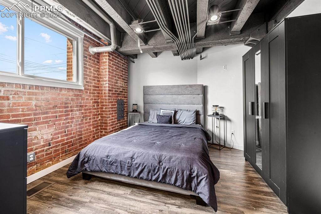 Bedroom featuring brick wall and wood finished floors
