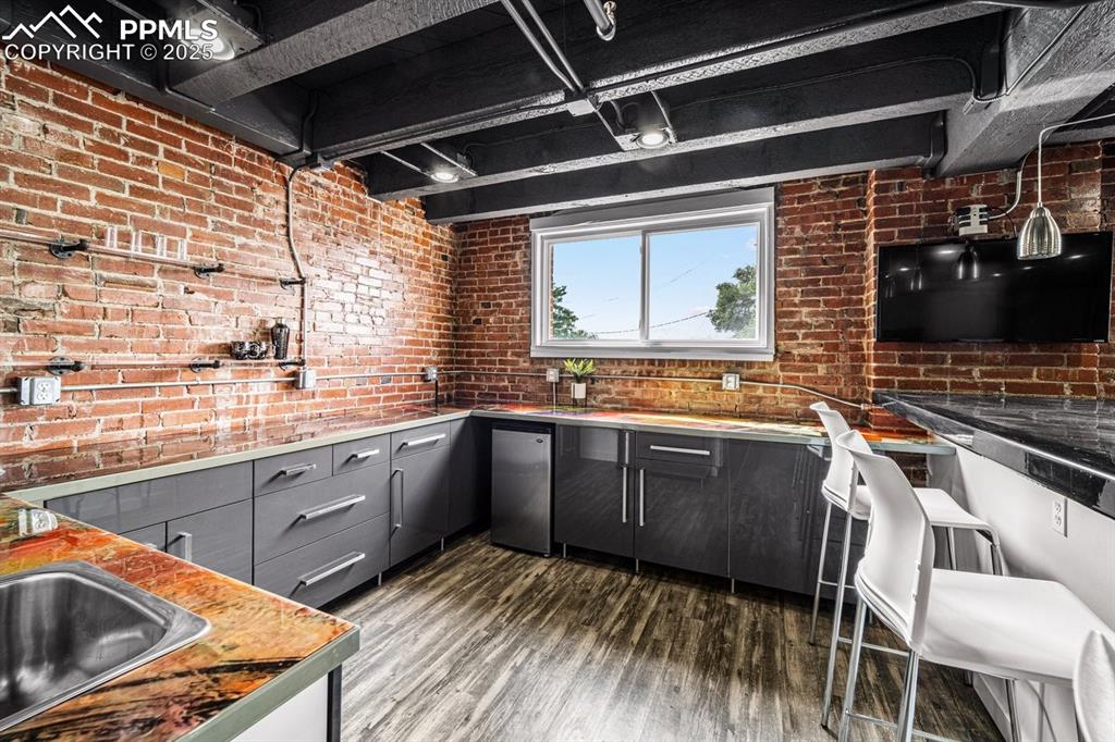 Kitchen with gray cabinets, dark wood-type flooring, brick wall, fridge, and light countertops