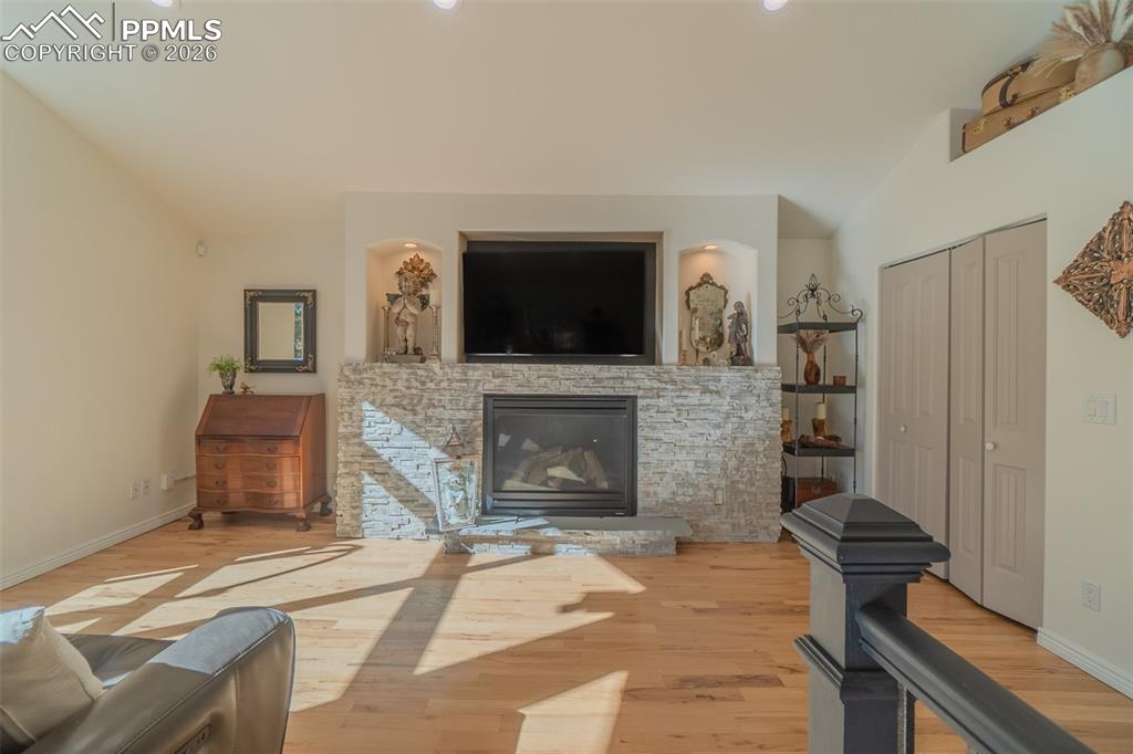 Living room with a stone fireplace, wood finished floors, lofted ceiling, and recessed lighting