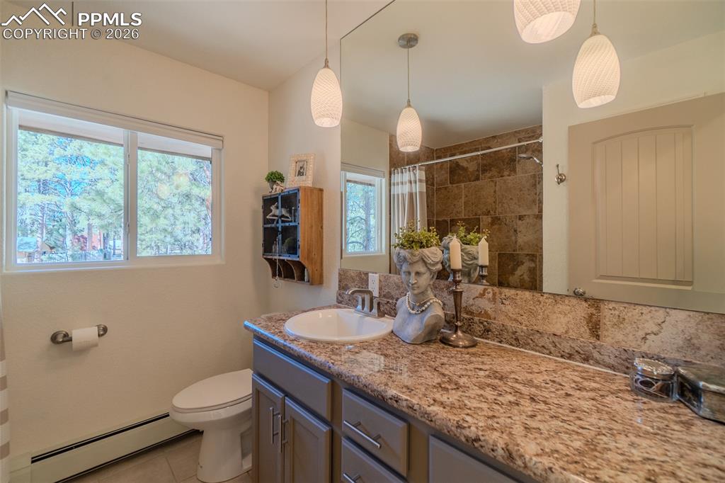 Full hall bathroom featuring curtained shower, a baseboard radiator, vanity, and light tile patterned flooring