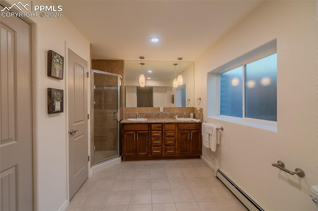 Lower Level Bathroom with double vanity, a baseboard radiator, light tile patterned floors, a shower stall, and recessed lighting