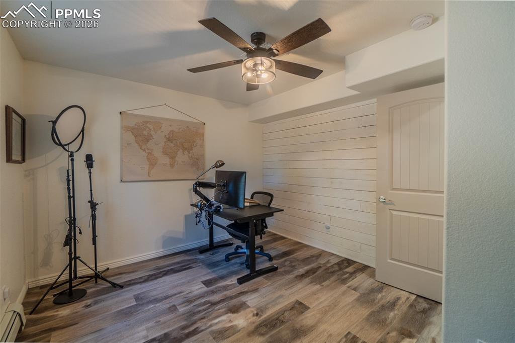 Currently used as a Home office with wood finished floors, a baseboard heating unit, ceiling fan, and wood walls
