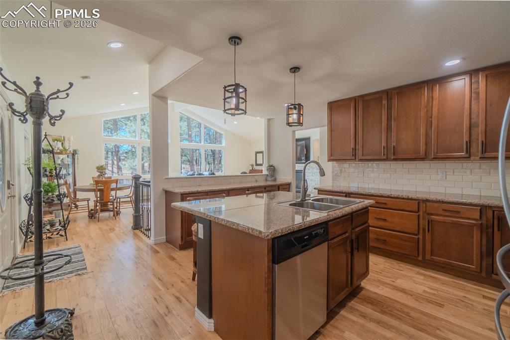 Kitchen with a center island with sink, dishwasher, backsplash, light wood-style flooring, and hanging light fixtures