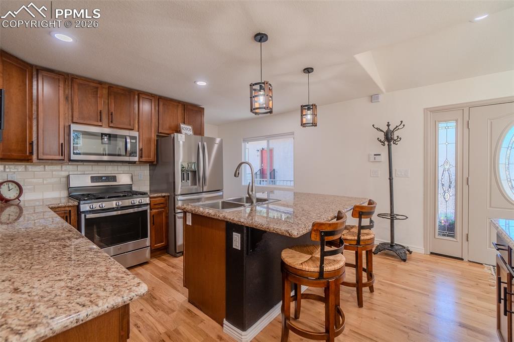Kitchen featuring stainless steel appliances, wood finish cabinets, a kitchen island with sink, and hanging light fixtures