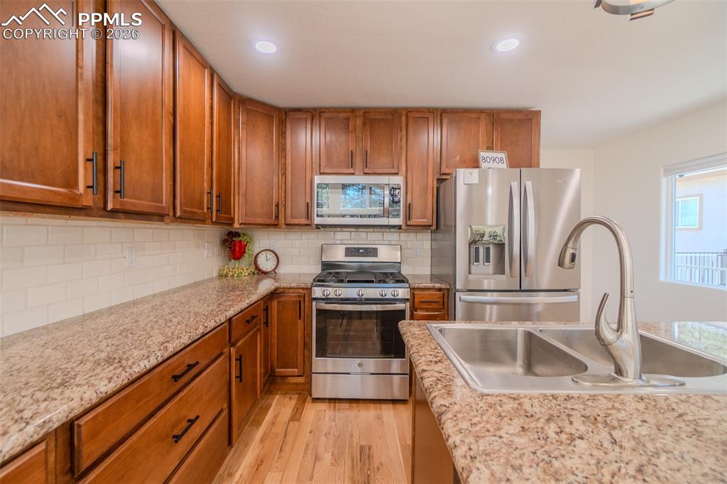 Kitchen featuring granite countertops, stainless steel appliances, wood finish cabinets, backsplash, light wood-style flooring, and recessed lighting