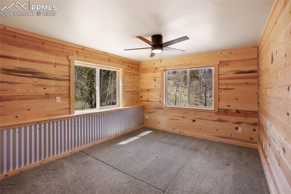 Primary bedroom with pine paneling, metal accents, carpet and ceiling fan