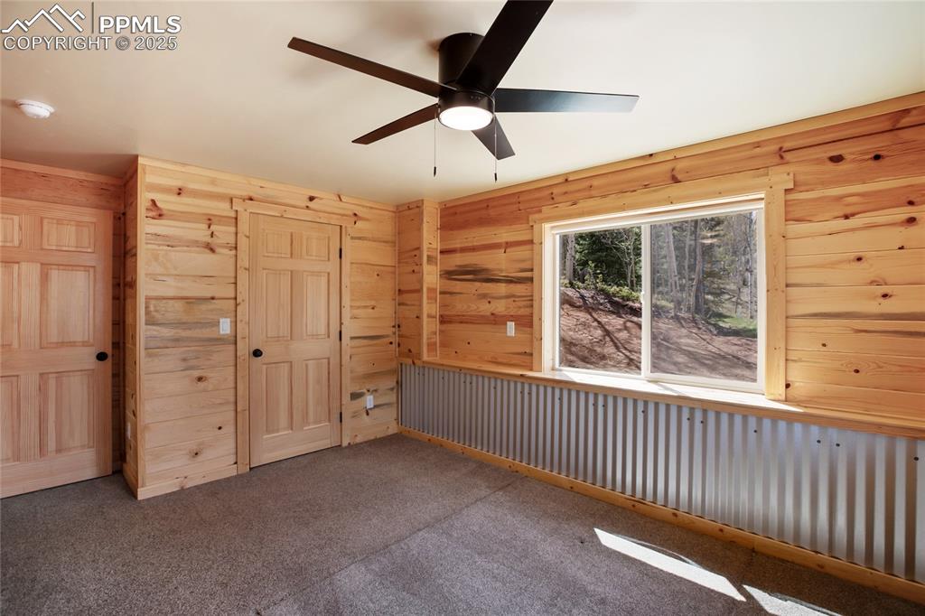 Unfurnished bedroom featuring wooden walls, carpet, a closet, and a ceiling fan