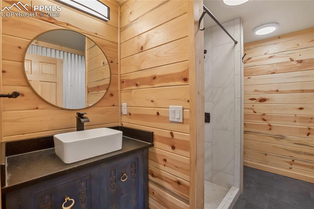 Main level full bathroom with wood walls, vanity, and a walk in shower