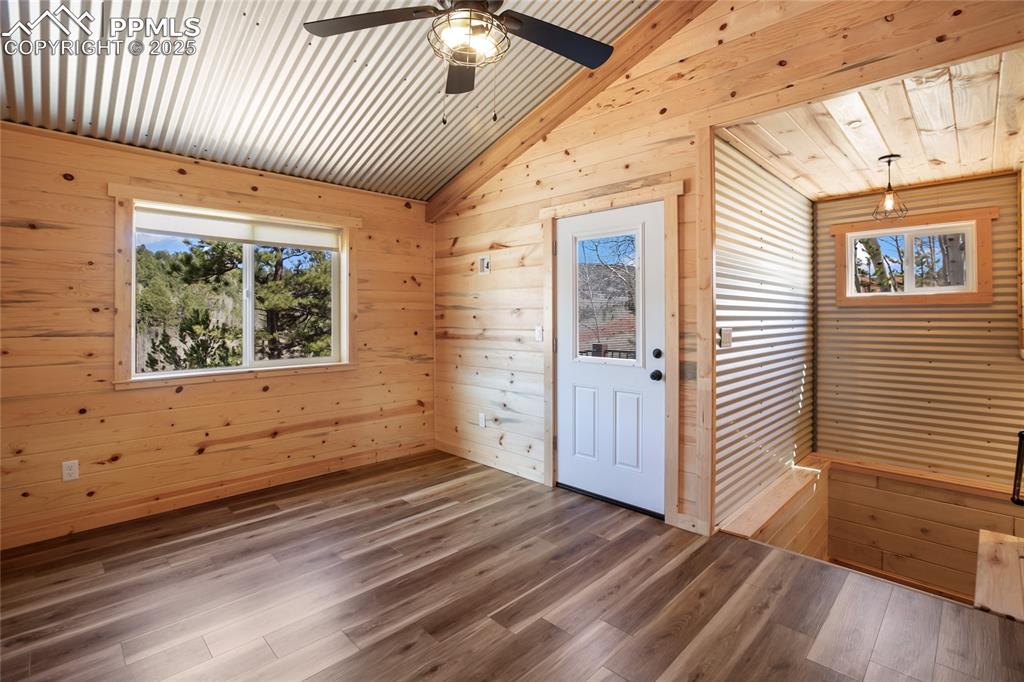 Unfurnished room with wooden walls, plenty of natural light, vaulted ceiling, wood finished floors, and ceiling fan