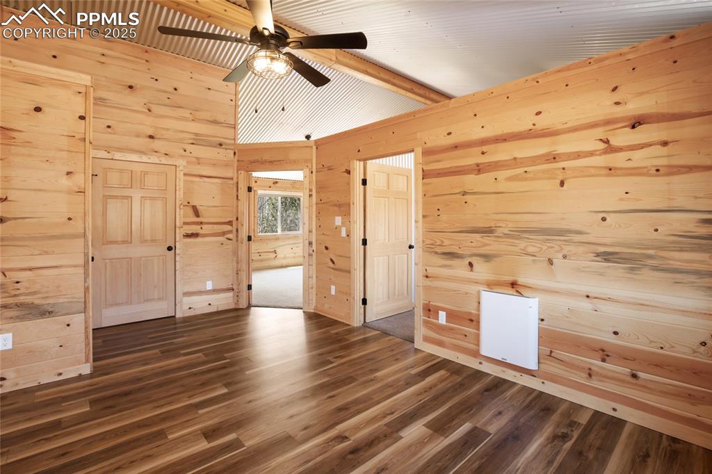 Unfurnished bedroom featuring wood walls, dark wood finished floors, and a ceiling fan