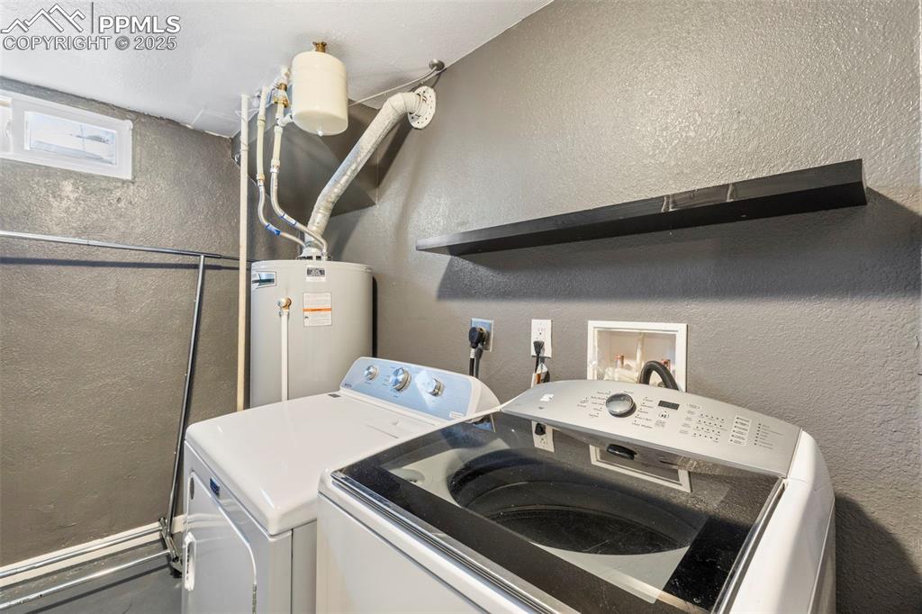 Laundry area featuring a textured wall, separate washer and dryer, and water heater