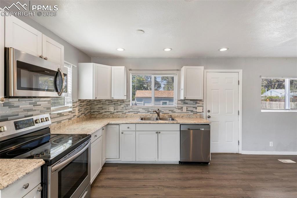 Kitchen with appliances with stainless steel finishes, white cabinetry, backsplash, dark wood/laminate-type flooring, and recessed lighting