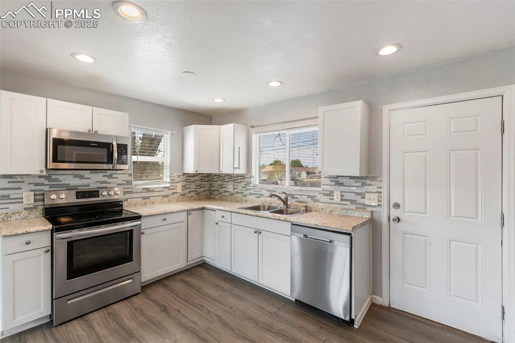 Kitchen featuring appliances with stainless steel finishes, white cabinets, dark wood/laminate-type flooring, backsplash, and recessed lighting