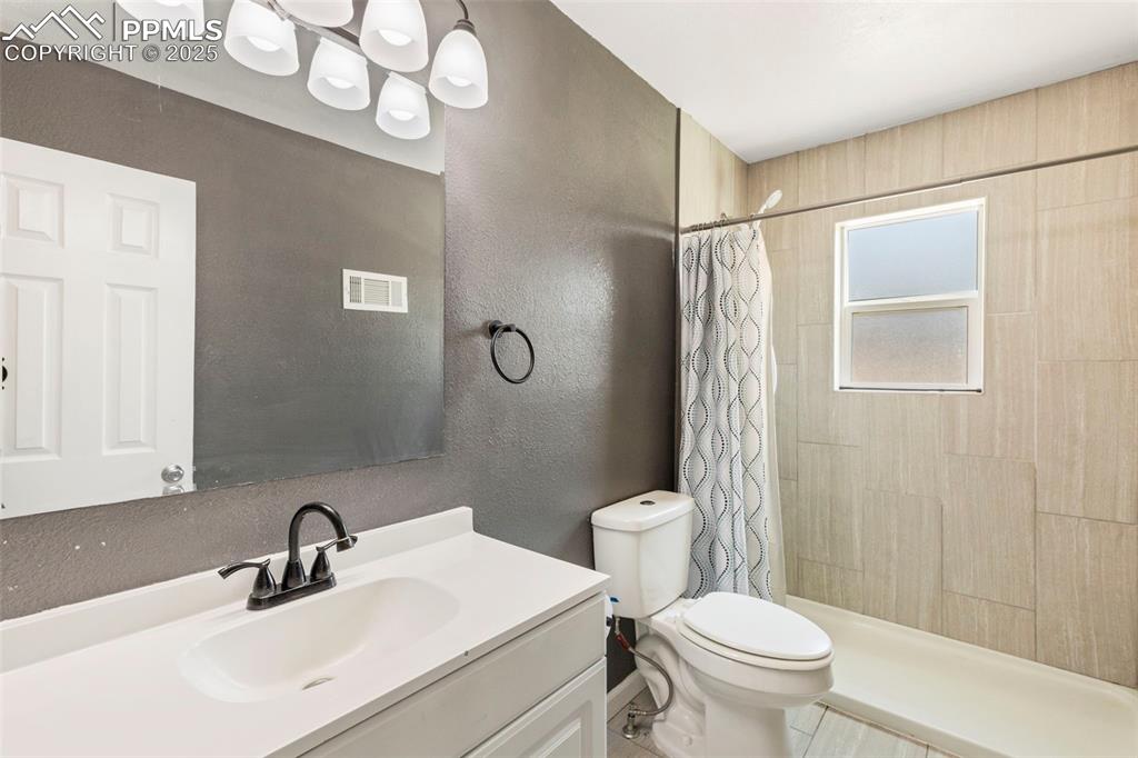 3/4 bath featuring a textured wall, vanity, and a stall shower