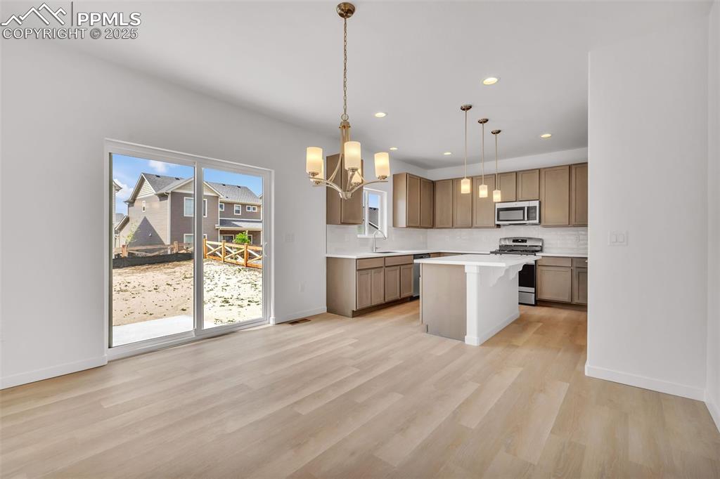Kitchen featuring a kitchen breakfast bar, a chandelier, stainless steel appliances, tasteful backsplash, and decorative light fixtures
