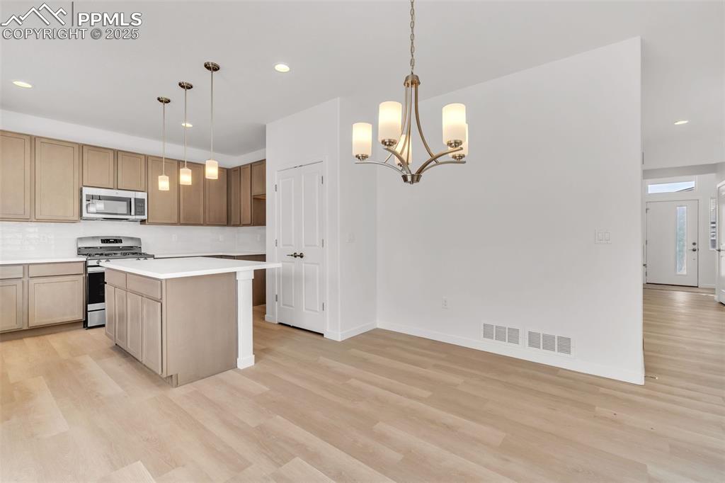 Kitchen with recessed lighting, appliances with stainless steel finishes, hanging light fixtures, light countertops, and a kitchen island
