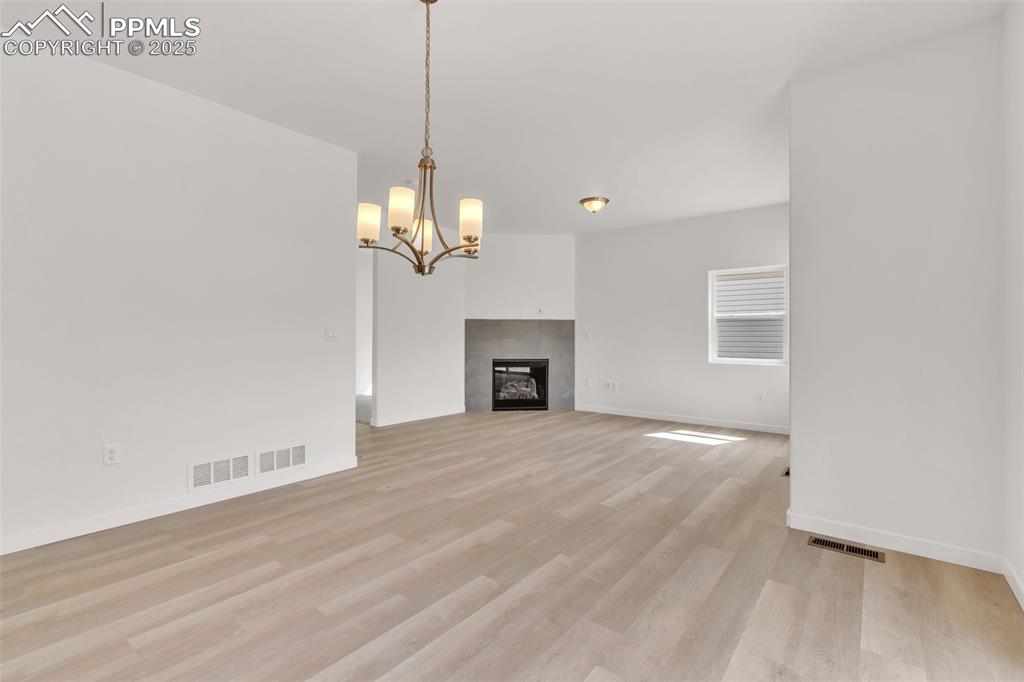 Unfurnished living room featuring a chandelier, a tile fireplace, and light wood finished floors