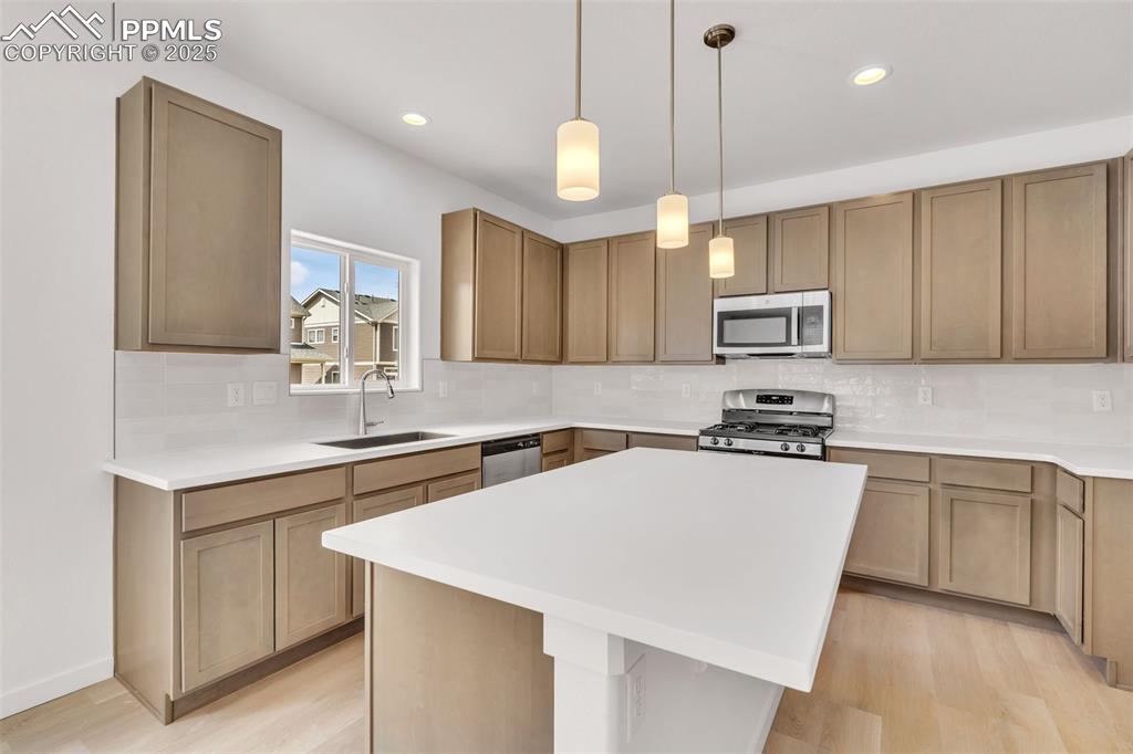 Kitchen featuring decorative light fixtures, backsplash, stainless steel appliances, a center island, and recessed lighting