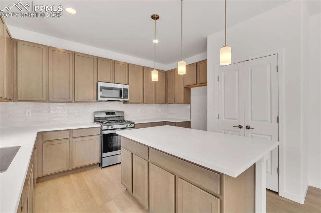 Kitchen featuring appliances with stainless steel finishes, light wood-type flooring, decorative light fixtures, decorative backsplash, and recessed lighting