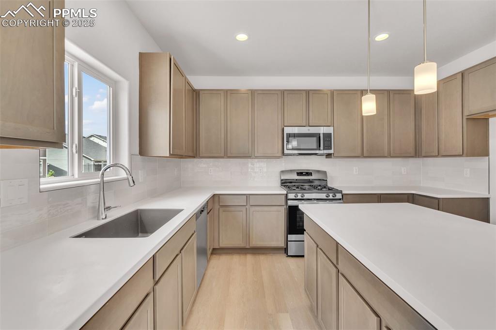 Kitchen featuring stainless steel appliances, backsplash, decorative light fixtures, light wood-style floors, and recessed lighting