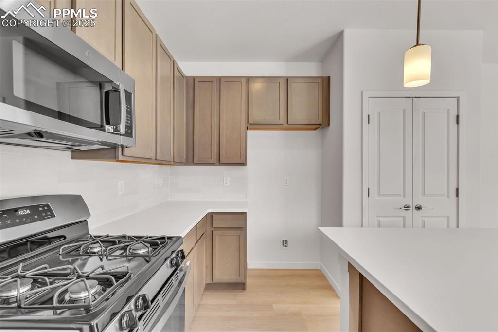 Kitchen with stainless steel appliances, pendant lighting, light wood finished floors, tasteful backsplash, and light stone countertops
