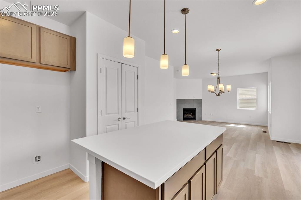 Kitchen with a center island, decorative light fixtures, a fireplace, light countertops, and light wood finished floors